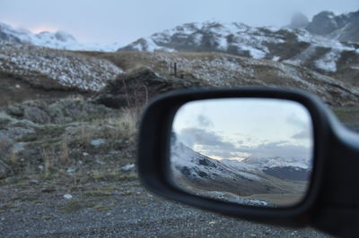 Close-up of side-view mirror against sky