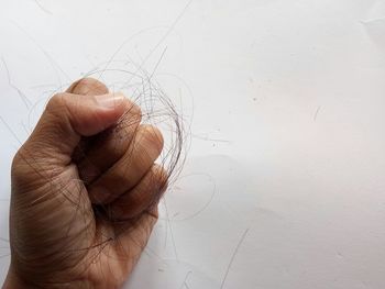 Close-up of hand holding hair against white wall