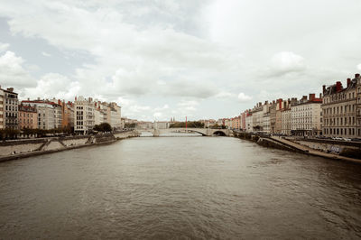 Buildings by river against cloudy sky