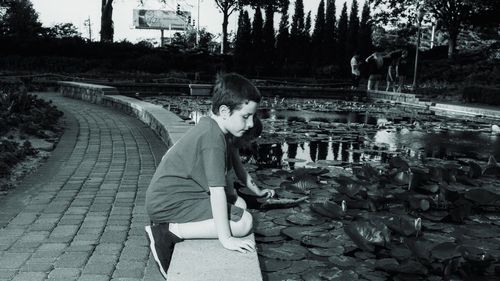 Rear view of boy sitting on bridge over lake