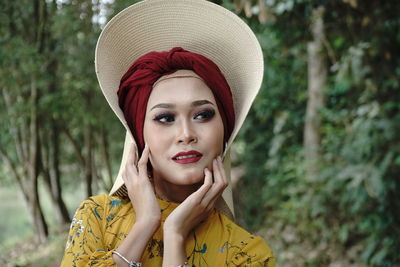 Woman looking away while wearing hat against trees