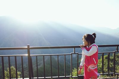 Girl standing by railing on balcony against mountains