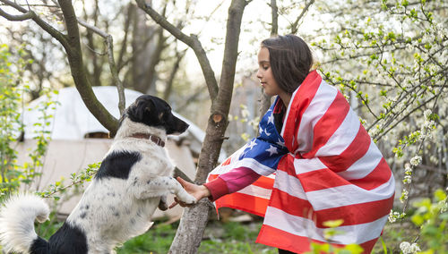 Girl with american flag crouching by dog in park