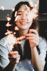 Smiling young woman holding sparklers at home