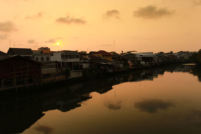 Reflection of houses in lake against sky during sunset