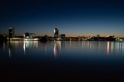 Illuminated buildings by lake against sky at night