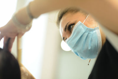 Female hair stylist at work wearing face mask while styling young gir