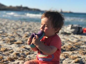 Close-up of boy biting shoe while sitting on sand at beach