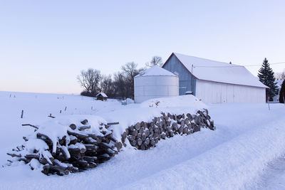 Piles of cut wood and farm buildings covered in fresh snow during a blue hour winter morning