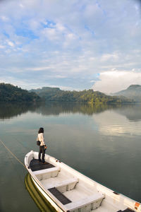 Rear view of man sitting on boat on lake against sky