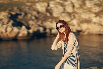 Smiling woman wearing sunglasses standing against water