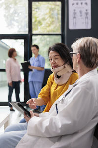 Portrait of young woman using mobile phone while sitting on bed at clinic