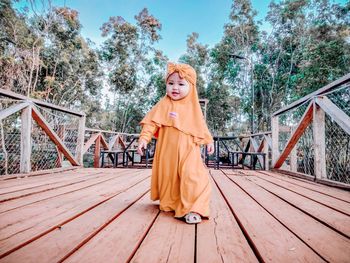 Portrait of woman standing on footbridge against trees