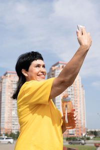 Portrait of smiling young man holding yellow while standing against sky