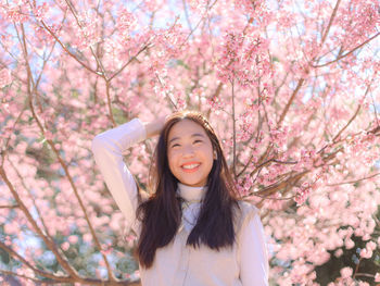 Portrait of smiling young woman standing by cherry blossom tree