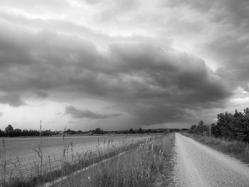 Dirt road amidst field against sky