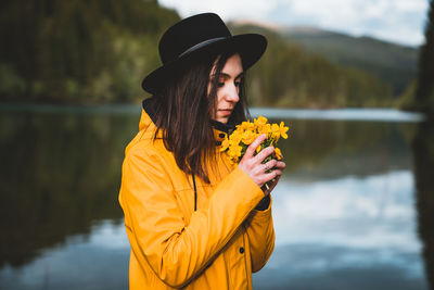 Woman smelling flowers while standing by lake