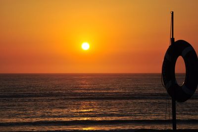 Silhouette lifebelt on pole at praia da costa nova against sky during sunset