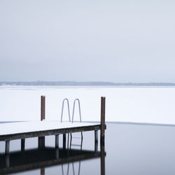 Pier by frozen lake against sky