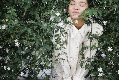 Relaxed woman standing with eyes closed amidst plants in backyard