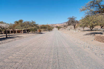 Road amidst trees against clear blue sky