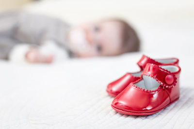 Baby girl lying down by red shoes on bed