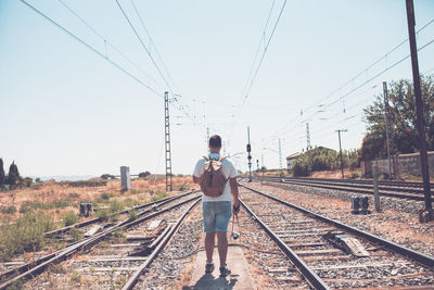 Rear view of man standing on railroad tracks against sky