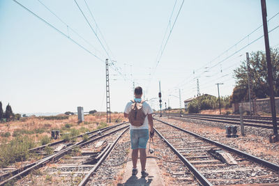 Rear view of man standing on railroad tracks against sky during sunny day