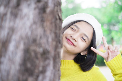 Portrait of smiling young woman against tree trunk