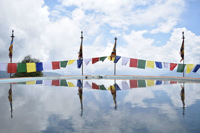 Reflection of colorful flags in water against cloudy sky