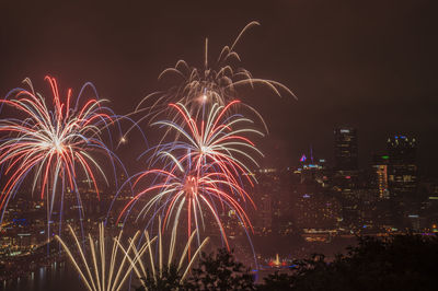 Firework display over city against sky at night