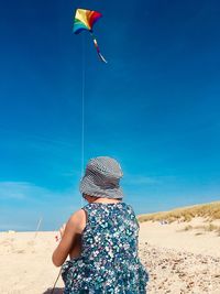 Rear view of girl wearing hat flying kite against sky