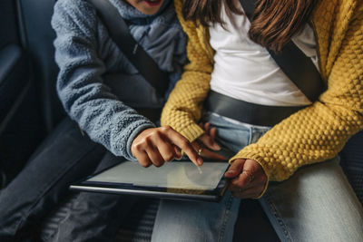 High angle view of girl using tablet pc with sister sitting in car