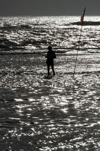 Silhouette man standing on sea shore against sky