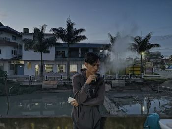 Young man drinking water in city against sky