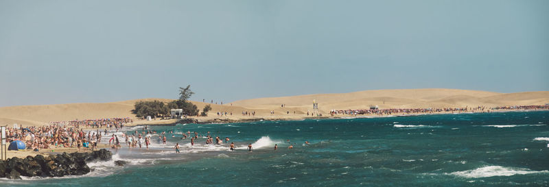 Panoramic view of people at beach against clear sky