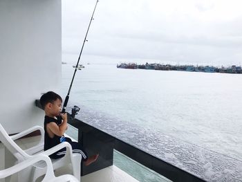 Cute boy fishing while sitting at balcony