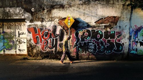Side view of man walking by graffiti on old wall