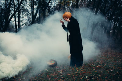 Man standing on snohalloween pumpkin head with scary face outdoorsw covered land