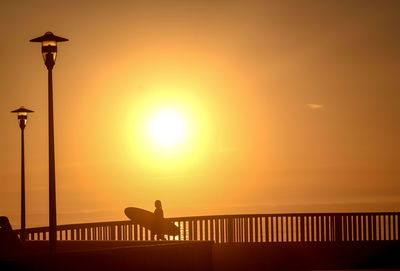 Silhouette man by railing against sky during sunset