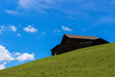 Low angle view of house on grassy hill against blue sky