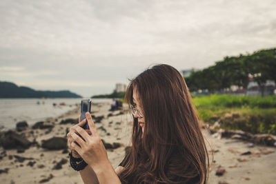 Side view of woman photographing while standing at beach