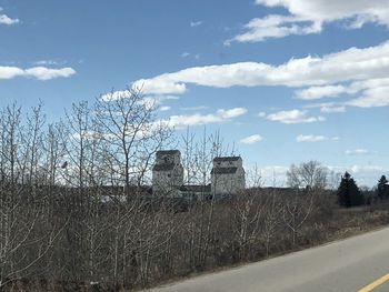 View of bare trees and buildings against cloudy sky