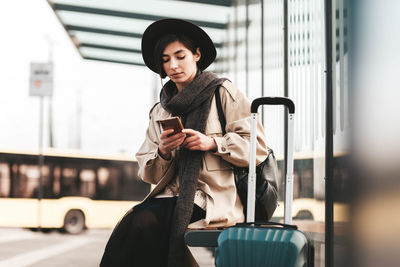 Pretty woman tourist uses a phone while sitting at a city bus stop