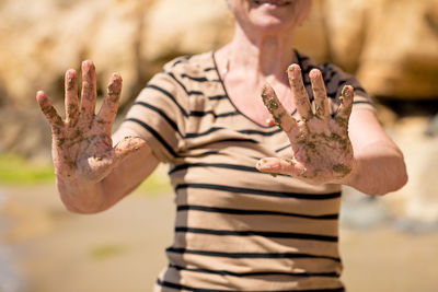 Elderly unrecognizable woman showing her palm hands covered in sand