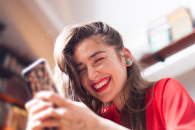 Low angle view of smiling woman using mobile phone at home