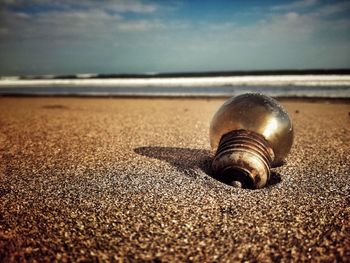 Close-up of abandoned light bulb on sand at beach against sky