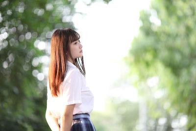 Young woman looking away while standing against tree