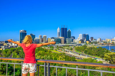 Rear view of woman with arms outstretched looking at buildings in city