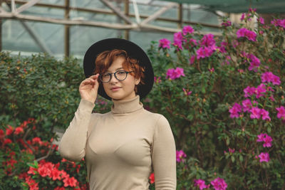 A beautiful plus size girl in eyeglasses and hat smiling among the green plants and flowers.